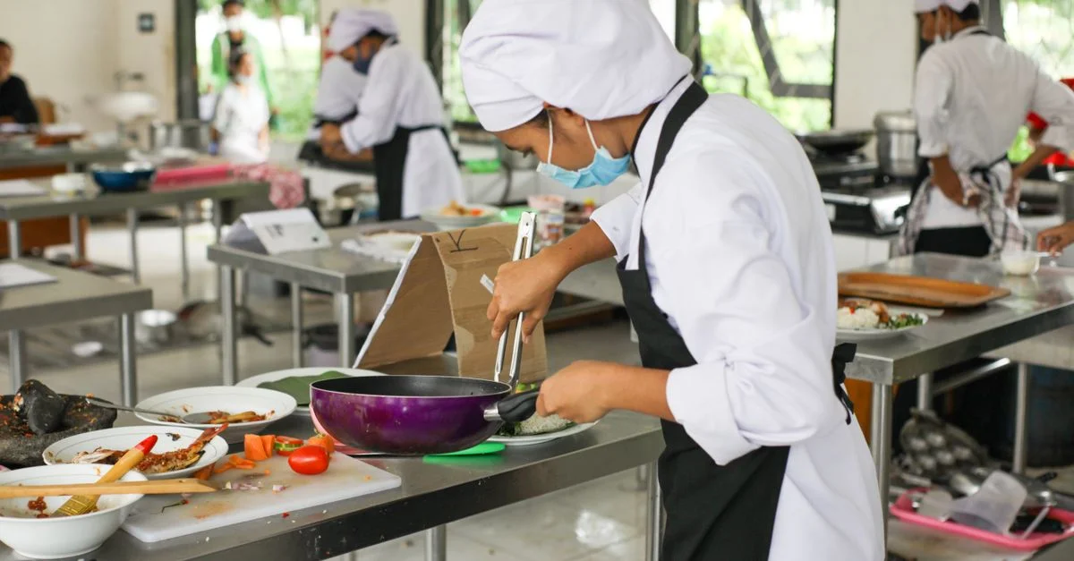 Des étudiants en cuisine en uniforme pratiquent leurs compétences culinaires dans un cadre de cuisine professionnel.