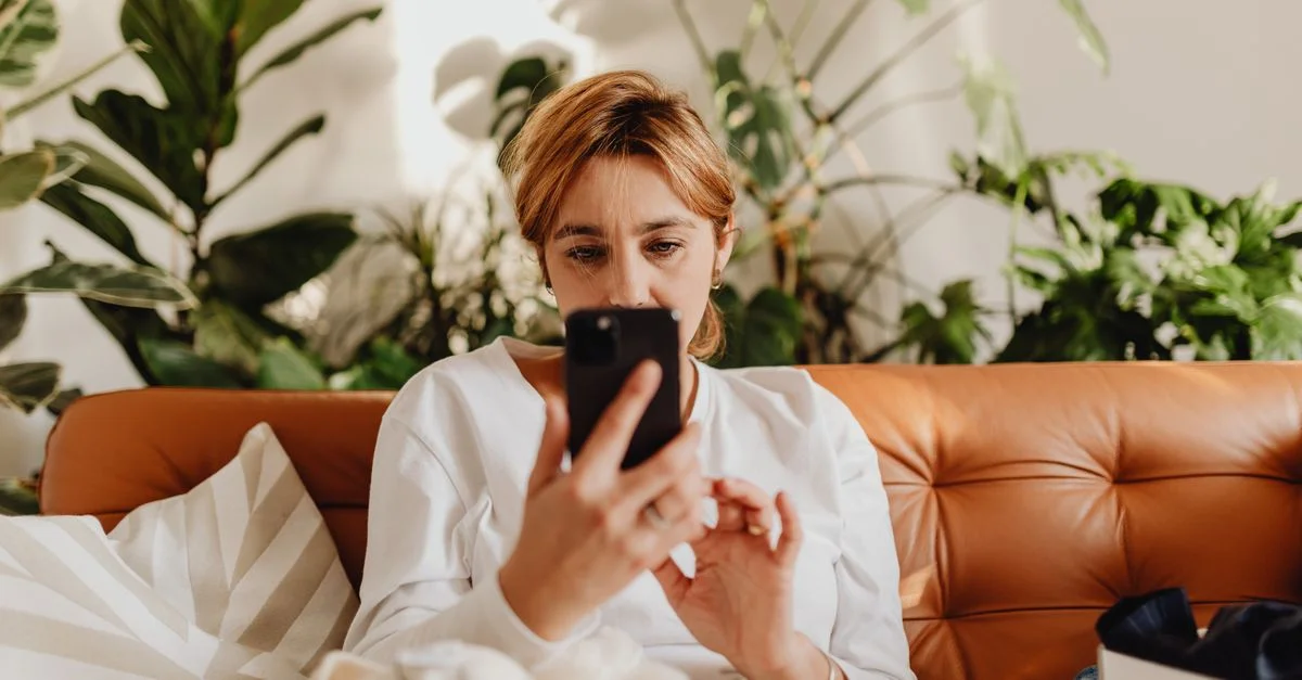 Femme dans un cadre décontracté, utilisant un smartphone sur un canapé avec des plantes d'intérieur.