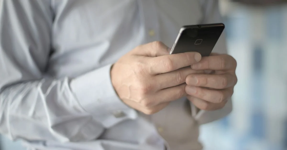 Gros plan sur un homme d'affaires utilisant un smartphone, mettant en avant des thèmes d'affaires et de communication.